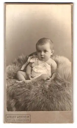 Fotografie Wertheim, Berlin, Oranienstrasse, Portrait Kleinkind im weissen Leibchen auf einem Fell sitzend