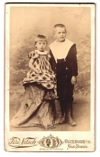Fotografie Ferd. Nitsch, Osterode i. H., Neue-Str., Portrait Bruder und Schwester im Anzug und kariertes Kleid