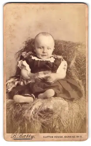 Fotografie B. Barry, London, Barking Roead, Portrait kleiner Junge Wiliam Georg Hary im Kleid auf einem Heuballen