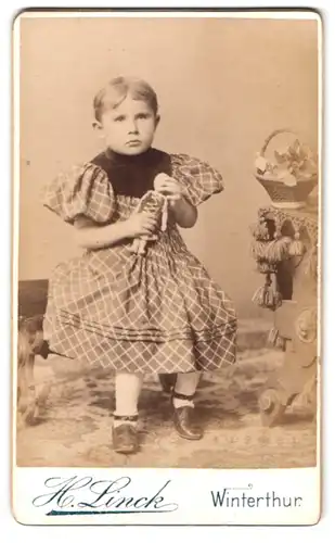 Fotografie H. Linck, Winterthur, St. Georgenstr., Portrait kleines Mädchen im karierten Kleid mit Puppe in der Hand