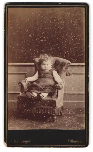 Fotografie V. Neininger, Villingen, Portrait kleines Kind im gehäkelten Kleid mit Locken im Kindersessel