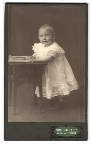 Fotografie Wilh. Müller, Wyk a /Föhr, Sandwall, Portrait kleines Mädchen im Kleid mit Bilderbuch