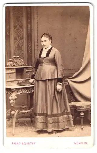 Fotografie Franz Neumayer, München, Neuhauserstr. 29, stämmige Dame im Kleid neben einem Holztisch