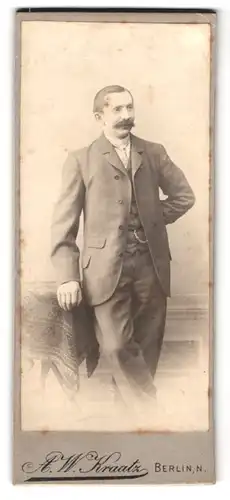 Fotografie A. W. Kraatz, Berlin, Herr mit dichtem Schnauzbart trägt Anzug und lehnt an einem Tisch