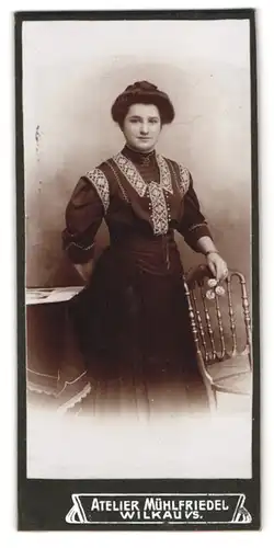 Fotografie Atelier Mühlfriedel, Wilkau i. S., Junge Dame mit dunklen Haaren trägt besticktes Kleid und posiert mit Stuhl
