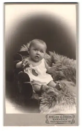 Fotografie G. Drees, Barmen, Heckinghauserstr. 168, Portrait süsses Kleinkind im weissen Hemdchen auf Fell sitzend