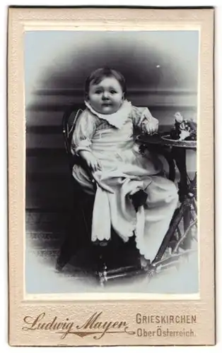 Fotografie Ludwig Mayer, Grieskirchen, Kleinkind in weissem Kleid mit Zierkragen sitzt an einem Tisch