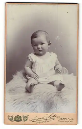 Fotografie August Lutz, Gera, Kleinkind in weissem Seidenlaibchen sitzt auf einem hellem Fell