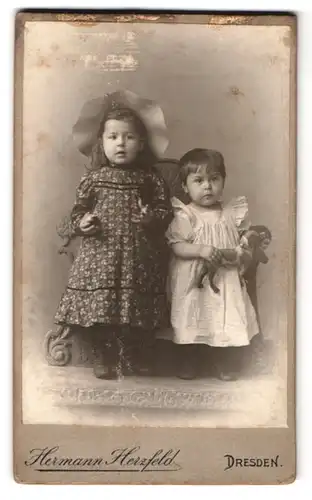 Fotografie Hermann Herzfeld, Dresden, Altmarkt, Portrait zwei bildhübsche kleine Mädchen mit Spielzeug in den Händen