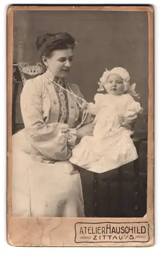 Fotografie Atelier Hauschild, Zittau i. S., Cirkus-Allee 4, Portrait stolze Mutter mit süsser tochter im Taufkleidchen