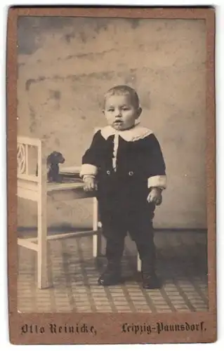 Fotografie Otto Reinicke, Leipzig-Paunsdorf, Portrait süsser kleiner Bube im niedlichen Anzug und Spielzeug auf dem Stuhl