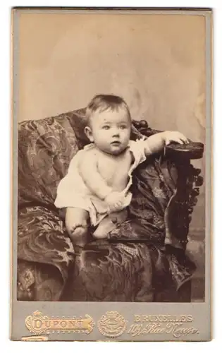 Fotografie Dupont, Bruxelles, 109 Rue Neuve, Portrait süsses Kleinkind im Hemdchen auf einem Sofa sitzend