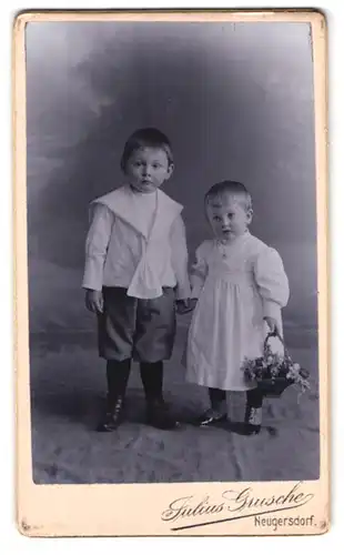 Fotografie Julius Grusche, Neugersdorf i /Sachs., Portrait hübsch gekleidetes Kinderpaar mit Blumenkorb