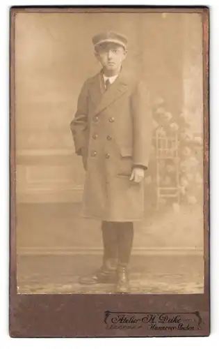 Fotografie H. Deike, Hannover-Linden, Deisterstrasse 7, Portrait junger Mann im Mantel mit Schirmmütze