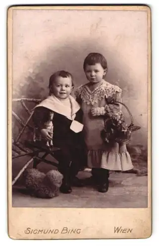 Fotografie Sigmund Bing, Wien, Goldschmidgasse 4, Portrait hübsch gekleidetes Kinderpaar mit Spielzeugpferd