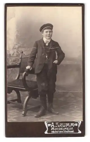 Fotografie A. Krumm, Mindelheim, Portrait halbwüchsiger Knabe im Anzug mit Schirmmütze