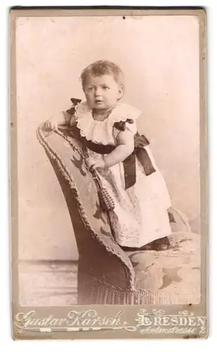 Fotografie Gustav Karsch, Dresden-N., Antonstrasse 2, Portrait kleines Mädchen im Kleid mit Rassel