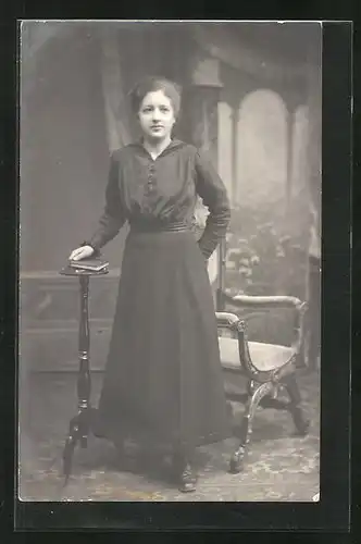 Foto-AK junge Frau steht mit Buch in der Hand an einem Stuhl