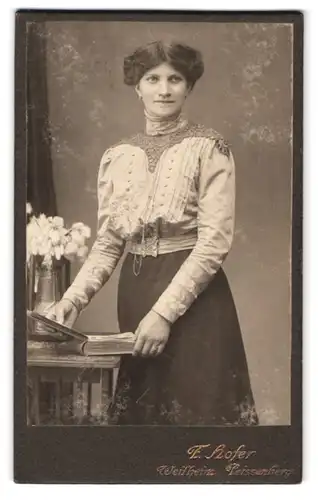 Fotografie F. Hofer, Weilheim, Portrait charmant lächelnde Frau mit Buch am Tisch stehend
