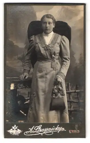 Fotografie A. Strassnicky`s Nachf., Enns, Portrait Dame im Trachtenkleid mit Handtasche und Schleife