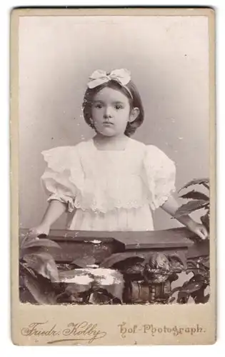 Fotografie Friedr. Kolby, Plauen i. V., Rädel-Str. 1, Portrait kleines Mädchen im weissen Kleid mit Haarschleife