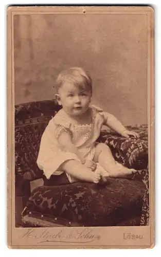 Fotografie H. Strube & Sohn, Löbau i. S., Blumenstr. 339, Portrait Kleinkind im Kleid sitzt auf einem Sessel