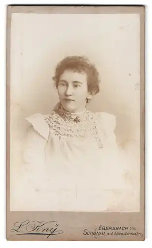 Fotografie L. Kny, Ebersbach i. S., Portrait Dame im weissen Kleid mit Locken und Brosche