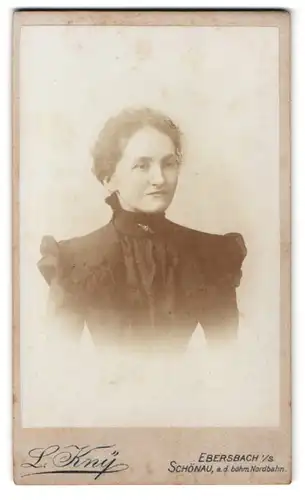 Fotografie L. Kny, Ebersbach i. S., Portrait junge Dame im schwarzen Kleid mit Locken, Brosche