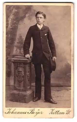 Fotografie Johannes Beyer, Zittau i. S., Portrait junger Knabe im schwarzen Anzug mit Hut posiert im Atelier
