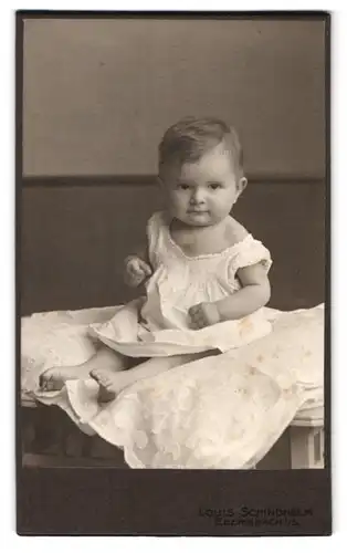 Fotografie Louis Schindhelm, Ebersbach i. S., Portrait Kleinkind im weissen Leibchen sitzt auf einer Decke