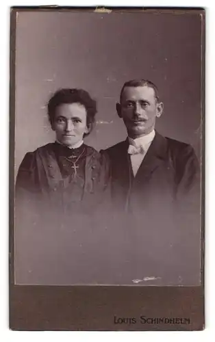 Fotografie Louis Schindhelm, Ebersbach i. S., Portrait Eheleute im Anzug mit Fliege und Kleid mit Kreuzkette