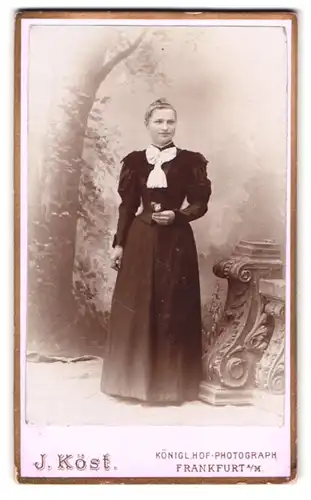 Fotografie J. Köse, Frankfurt a. M., Schäfergasse 17, Portrait junge Frau im schwarzen Kleid vor einer Studiokulisse