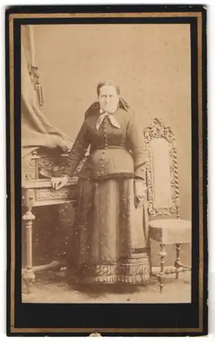 Fotografie J. F. Klinger, Braunau, Stadtgraben 318, Portrait ältere Frau im Kleid mit Schleife steht im Atelier