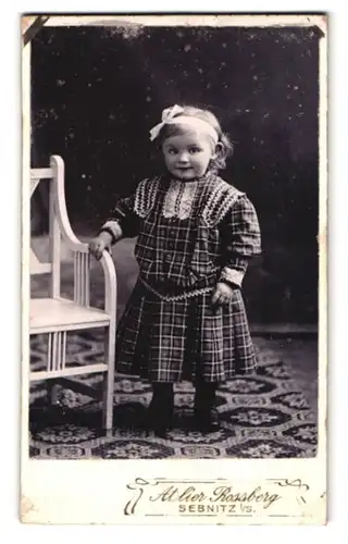 Fotografie Atelier Rossberg, Sebnitz i. S., Portrait kleines Mädchen im karierten Kleid mit Haarschleife