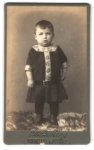 Fotografie Otto Döling, Bornstedt, Portrait Kleinkind im Kleid mit Mustern steht auf einem Fell