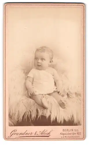Fotografie Grundner & Abich, Berlin, Köpenickerstr. 62, Portrait Kleinkind im Leibchen auf einem Fell sitzend