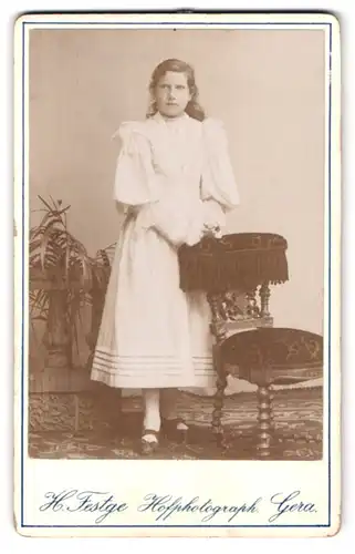 Fotografie H. Testge, Gera, Ecke der Humboldstr., Portrait junge Frau im weissen Kleid lehnt an einem Stuhl