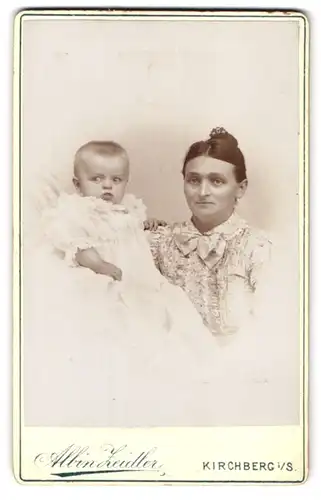 Fotografie Albin Zeidler, Kirchberg i. S., Portrait Mutter im hellen Kleid mit Schleife zeigt ihr Kleinkind
