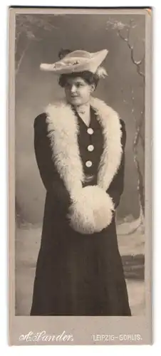 Fotografie A. Sander, Leipzig, Portrait junge Frau im schwarzen Kleid mit Pelzstola und Muff vor einer Winterlandschaft