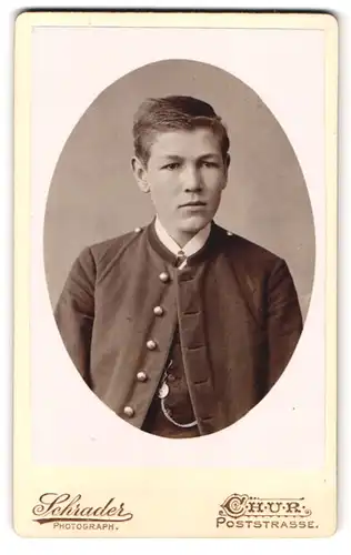 Fotografie Schrader, Chur, Poststrasse, Portrait junger Knabe im landes üblicher Jacke mit schweizer Anhänger