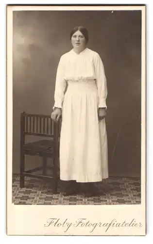 Fotografie Floby, Ort unbekannt, Portrait Dame im weissen Kleid steht neben einem Stuhl im Atelier