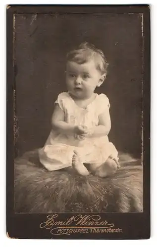 Fotografie Emil Winzer, Potschappel, Tharandterstr., Portrait Kleinkind im weissen Kleid auf einem Fell sitzend