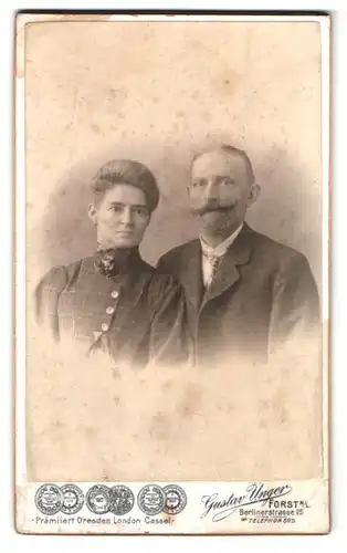 Fotografie Gustav Unger, Forst N. L., Berlinerstr. 25, Portrait Ehepaar im karierten Anzug und Kleid mit Brosche