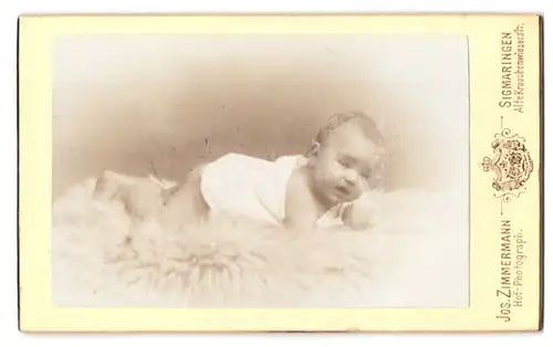 Fotografie Jos. Zimmermann, Sigmaringen, alte Krauchenwieserstr., Portrait Kleinkind im weissen Leibchen liegt auf Fell