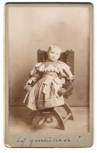 Fotografie Fotograf und Ort unbekannt, Portrait Mädchen Ilse im Kleid mit grosser Schleife sitzt im Stuhl