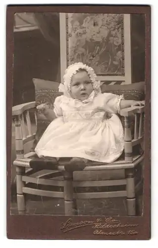 Fotografie Samson & Co., Hildesheim, Almsstr. 15a, Baby im weissen Nachthemd sitzend auf einem Stuhl