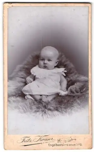 Fotografie Fritz Kauser, Hannover, Engelbosteldamm 6, Baby im weissen Kleid sitzend auf einem Fell
