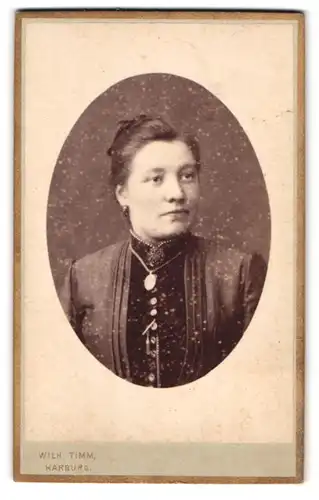 Fotografie Wilh. Timm, Harburg, Lindenstr. 1, Portrait elegant gekleidete Frau mit Amulettkette und Brosche am Kragen