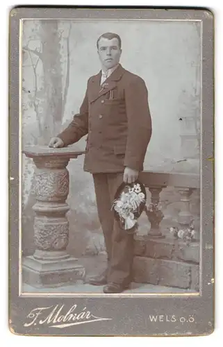 Fotografie F. Molnar, Wels, Westbahnstr. 10, Portrait Herr im Anzug mit Blumenhut und eingesteckten Zigarren