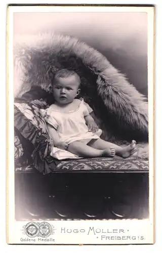 Fotografie Hugo Müller, Freiberg i. S., Fischerstr. 29, Portrait kleines Kind im weissen Kleid auf einem Sofa sitzend